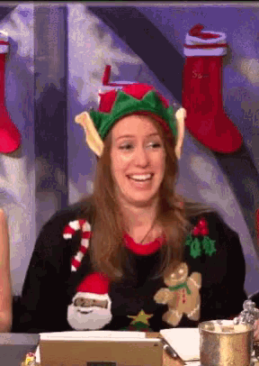 a woman wearing a christmas sweater and elf hat smiles