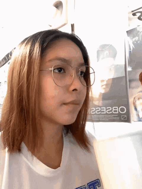 a girl wearing glasses is standing in front of a poster that says ob22e2i