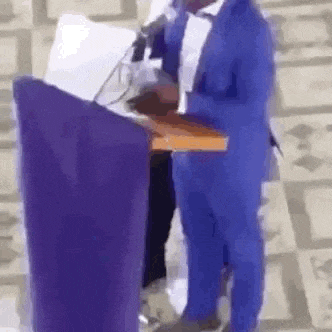 a man in a blue suit is standing at a podium holding a bible and a microphone .