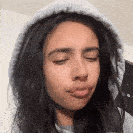 a woman wearing a grey hoodie is making a funny face .
