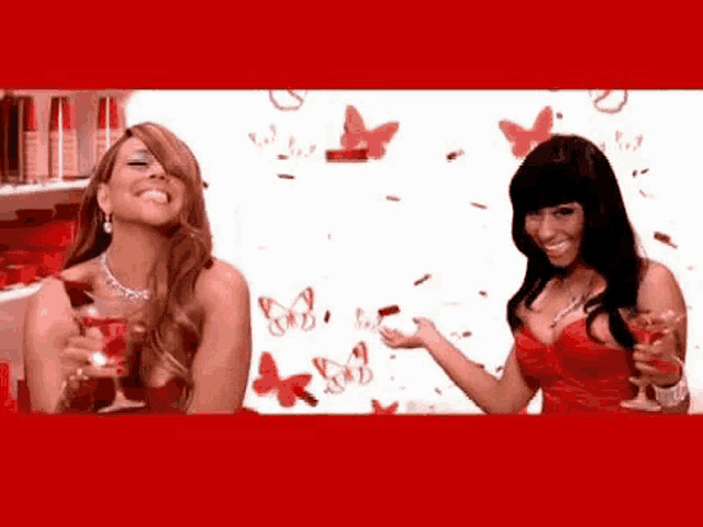 two women in red dresses are standing next to each other holding wine glasses in front of red butterflies .