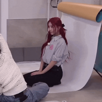 a woman with red hair is sitting on the floor in front of a white wall