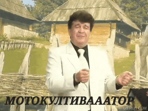 a man in a white suit and tie is dancing in front of a fence with the words motokultivaaator written on it