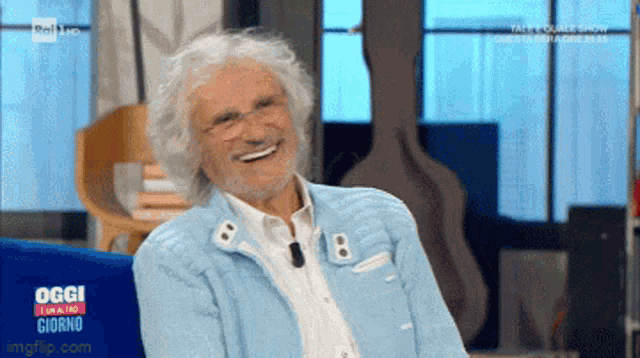 a man in a light blue jacket is smiling on a tv show