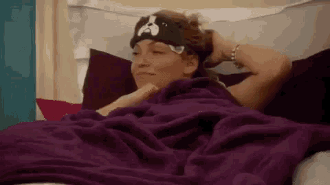a woman is laying in a bed with a purple blanket and a dog headband on her head .
