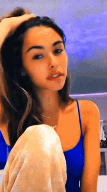 a young woman in a blue tank top is sitting on a bed .