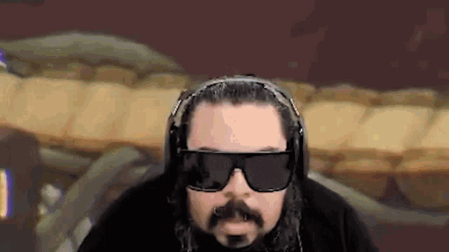 a man with a beard wearing sunglasses and headphones looks at the camera