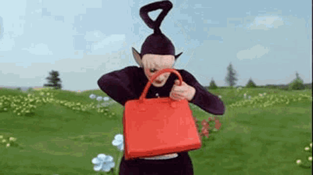 a cartoon character from the teletubbies is holding a red purse in a field .