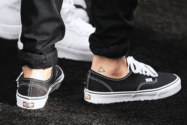 a person wearing a pair of black vans shoes with a triangle tattoo on their ankle