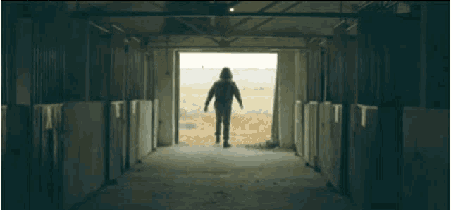 a man in a hooded jacket is walking out of a barn door