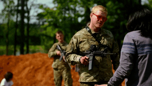 a man in a military uniform holds a gun while talking to a woman