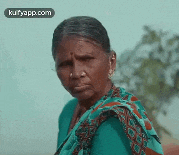 an elderly woman wearing a nose ring and a green saree is making a funny face .