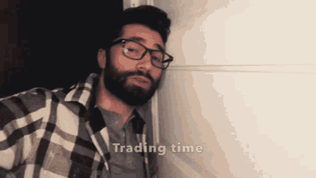 a man with glasses and a beard is leaning against a wall with the words trading time written above him
