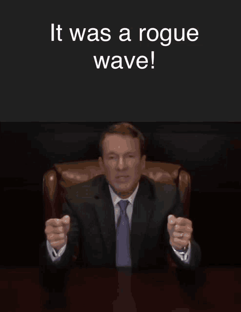 a man in a suit and tie sitting at a desk with the words " it was a rogue wave " behind him