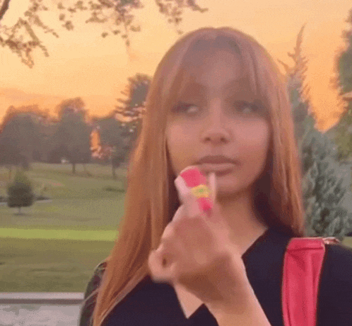 a woman is holding a lollipop in her hand in front of a park .