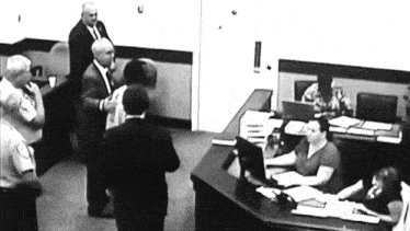 a man in a suit stands in front of a woman sitting at a desk
