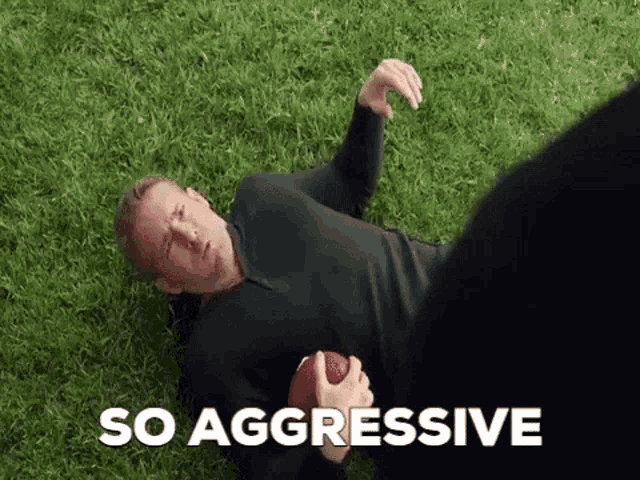 a man is laying on the grass holding a football and a person is standing behind him .