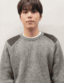 a young man wearing a grey sweater and earrings is looking at the camera .
