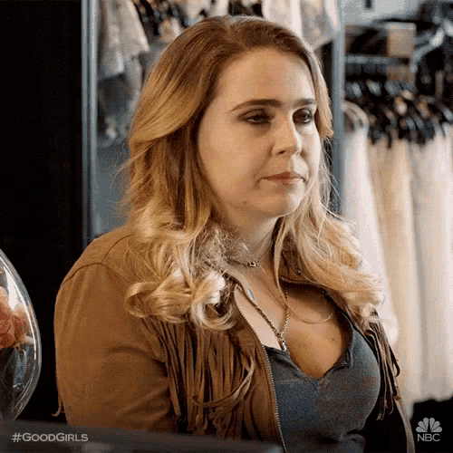a woman wearing a fringed jacket and a necklace is sitting in front of a rack of clothes .