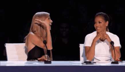 two women are sitting at a table with microphones in front of them and laughing .