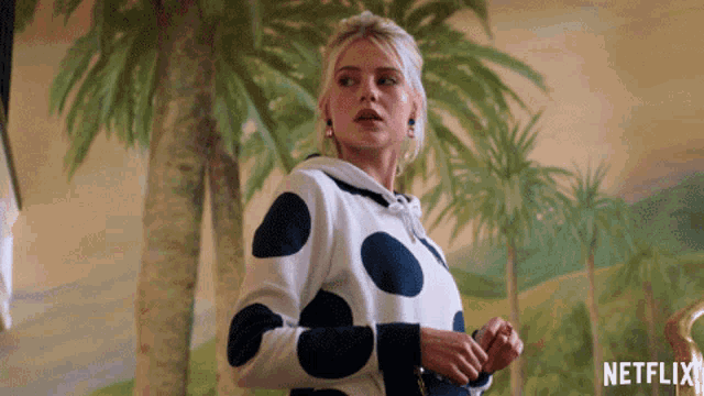 a woman wearing a polka dot sweater is standing in front of a netflix logo
