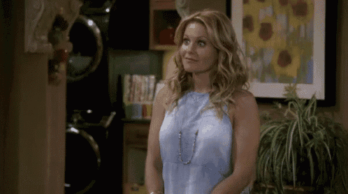 a woman in a blue tank top is standing in front of a painting of sunflowers .
