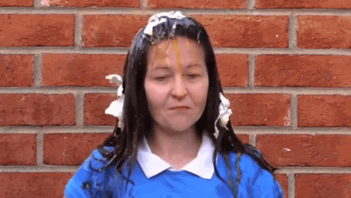 a woman with whipped cream on her face is standing in front of a brick wall ..