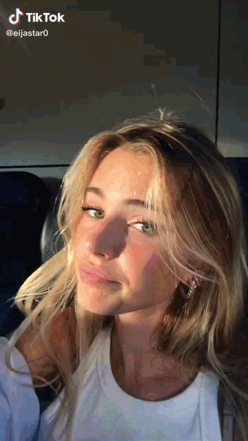 a woman with long blonde hair is wearing a white tank top and earrings