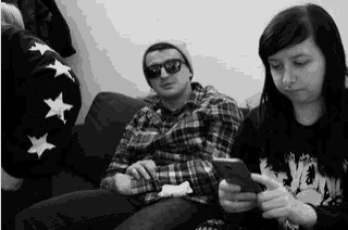 a man and a woman are sitting on a couch looking at a cell phone .