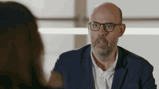 a bald man with glasses and a beard looks at a woman
