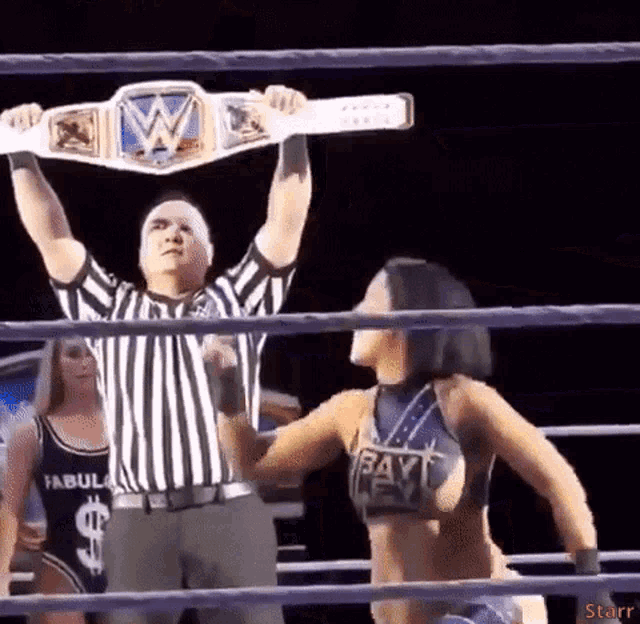 a referee is holding up a wrestling championship belt over a wrestler