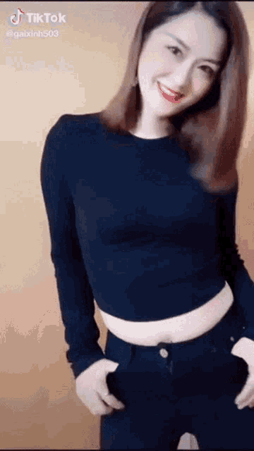 a woman in a black crop top and black jeans is smiling and looking at the camera .