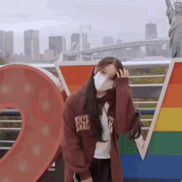 a woman wearing a mask is standing in front of a large rainbow colored sign