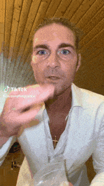 a man wearing a white suit and a cross necklace has a tiktok sticker on his face