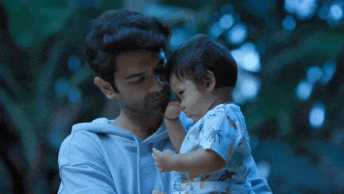 a man holds a baby in his arms and the baby is looking at the camera