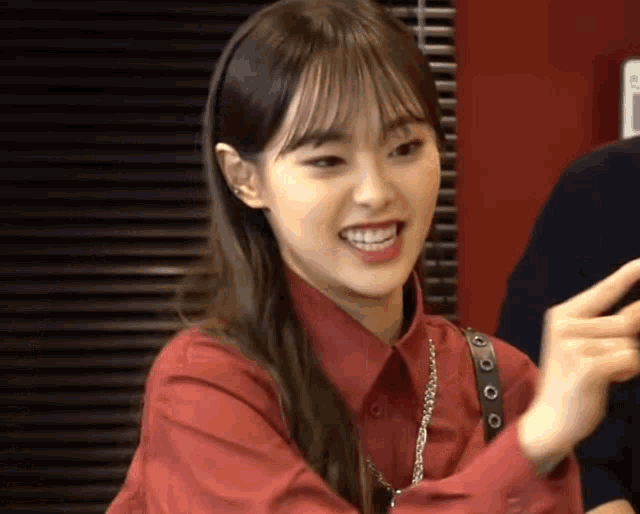 a young woman in a red shirt is smiling and making a peace sign .