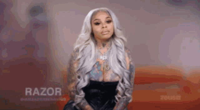 a woman with long white hair and a lot of tattoos on her body is standing in front of a red background .