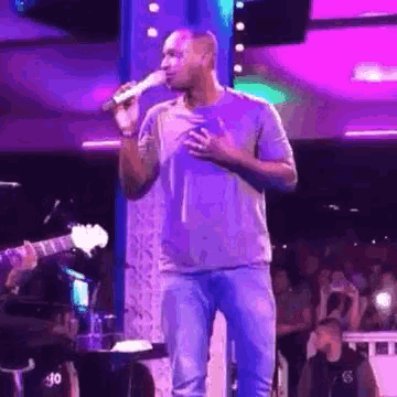 a man is singing into a microphone while standing on a stage in front of a crowd .