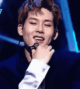 a young man is singing into a microphone while wearing a black suit and white shirt .