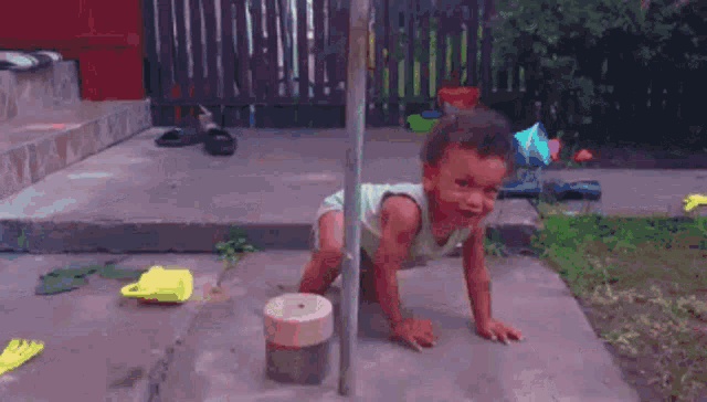 a baby is crawling on the ground in front of a wooden pole