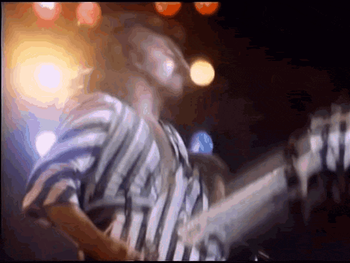 a man in a striped shirt is playing a bass guitar on stage .