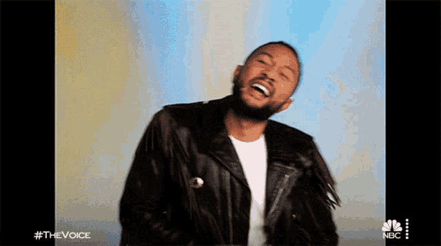 a man in a black leather jacket is laughing in front of a blue background