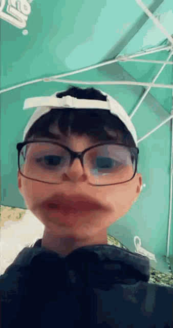 a young boy wearing glasses and a white hat makes a funny face .