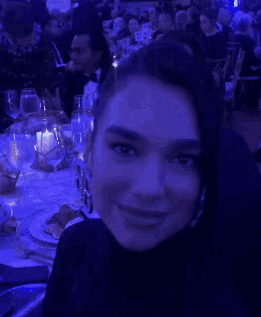 a woman in a black turtleneck is smiling in front of a table with plates of food and glasses of wine ..