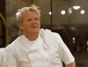 a man in a white chef 's uniform is dancing in a kitchen .
