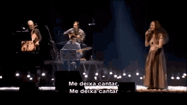 a woman is singing into a microphone on stage while a man plays a violin .