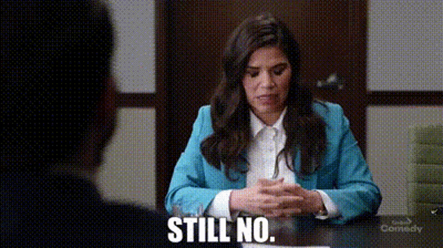 a woman in a blue jacket is sitting at a table with a man and says `` still no . ''