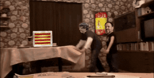 two men are standing in front of a laptop with a spanish flag on the screen