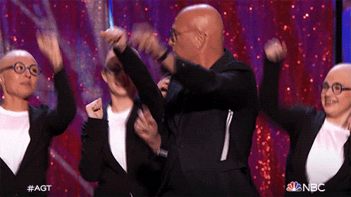a group of bald people are dancing on a stage with their arms in the air .