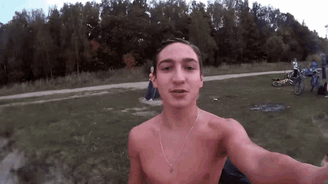 a shirtless man takes a selfie in a park